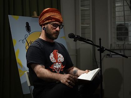 A poet reads from his book in a quiet, focused performance.