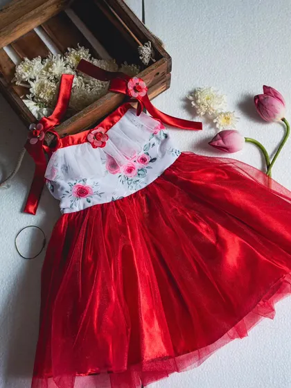 This stunning red and white party dress is a showstopper. It combines a floral print bodice with a voluminous red tulle skirt, accented with satin ribbon straps and floral details for a truly enchanting look.