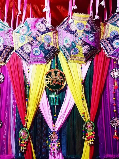 A Mehndi ceremony should be as colorful as the love story it celebrates. This vibrant backdrop uses multi-colored drapes and traditional Rajasthani umbrellas to create a joyful and picture-perfect setting for the bride-to-be.