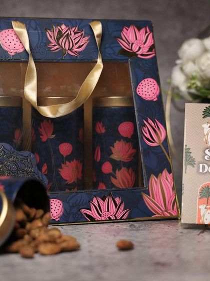 A beautiful navy blue and pink lotus-themed dry fruit box. The window allows a peek at the goodies inside, and the design is quintessentially festive.