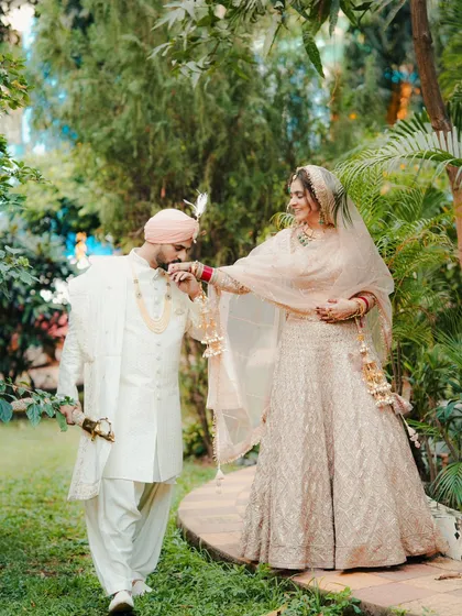 A romantic moment in a lush garden. The groom gently kisses his bride's hand, a classic pose that we love to capture for our Punjabi wedding couples.