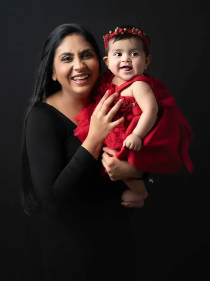 A mother and her baby girl, both sharing a beautiful, happy smile. The vibrant red dress on the little one adds a delightful splash of color to this classic portrait.