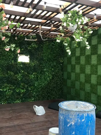 The pergola project during installation. You can see how the space is coming together with the wooden floor, patterned green wall, and hanging plants.