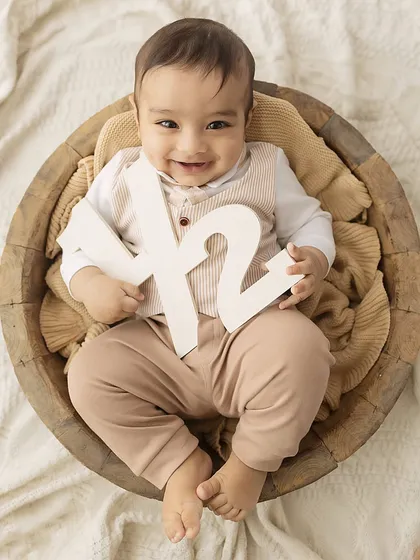 A classic 6-month milestone portrait, with the baby sitting in a rustic wooden bowl holding a "1/2" sign to mark his half-birthday.