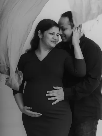 An intimate black and white portrait that feels like a classic painting. The gentle embrace, the soft fabric floating by, and the tender expressions all come together to create a deeply romantic and artistic maternity photograph.