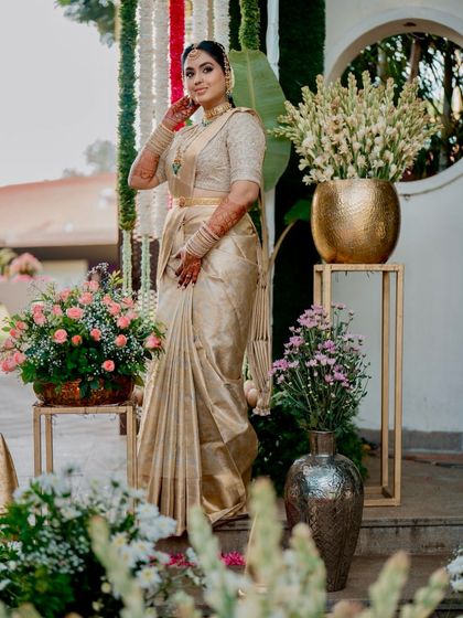A full-length portrait of a bride in a magnificent golden Kanchipuram saree. The saree's rich texture and the blouse's detailed embroidery create a regal and unforgettable bridal look.