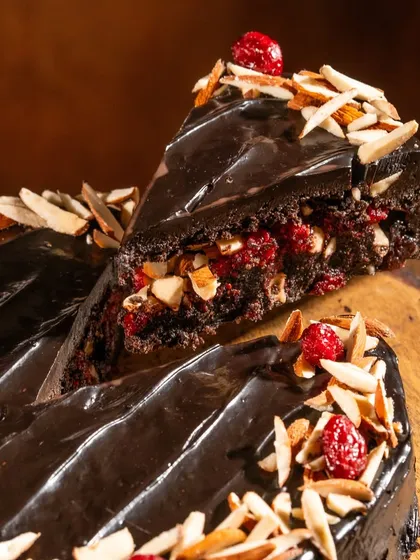 Here’s a close look at our star creation. You can see the rich, dense texture of the oat flour sponge, the bright pop of our house-made cranberry compote, and the generous topping of toasted almonds. The glossy finish comes from a silky vegan chocolate ganache we make with coconut milk.
