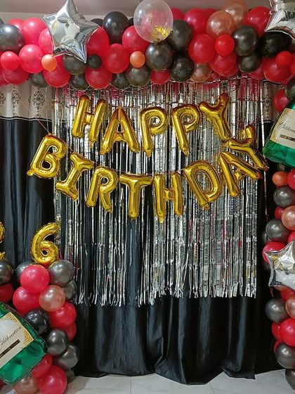 A fun and celebratory 26th birthday setup at home. This decoration includes a red and black balloon arch, a silver foil curtain, and champagne bottle foil balloons.