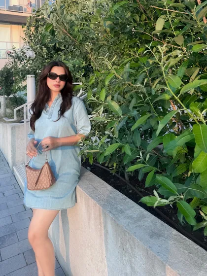 A golden hour shot featuring a Calvin Klein denim dress, Michael Kors bag, and Aldo wedges. I use natural lighting to highlight the complete outfit and create a warm, appealing summer vibe.