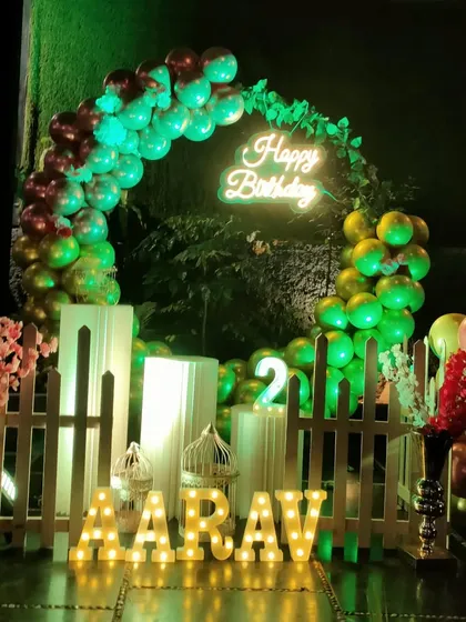 An outdoor evening party setup with a green balloon arch, neon sign, and marquee letters.