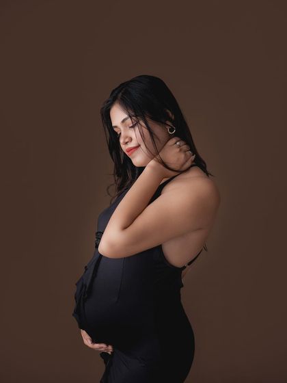 A classic, elegant maternity portrait against a simple brown backdrop. The side profile beautifully showcases the curve of the baby bump.