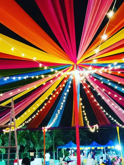 A close-up, upward view of the vibrant tent ceiling for a Navratri event. The dense layers of colorful fabric and bright lights create a spectacular effect against the night sky.