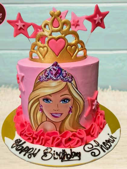 A lovely pink Barbie-themed cake. This design features an edible image of Barbie, a golden tiara, and star decorations, perfect for a fan of the iconic doll.