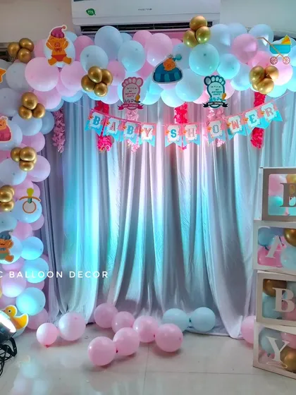 A playful baby shower backdrop with a pink and blue balloon arch, a 'Baby Shower' banner, and cute baby-themed cutouts along the top.