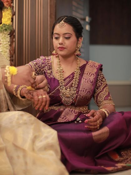 Madhu participating in a ceremony, her beautiful purple Kanchi silk saree adding to the sanctity of the moment.