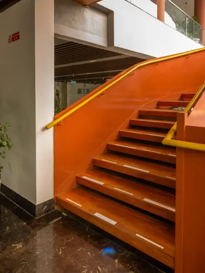A detailed view of the sculptural staircase at the Sona Vistaas Clubhouse. The choice of terracotta red and warm wood for the steps complements the earthy palette of the architecture, turning a functional element into a central piece of art that guides movement and defines the space.