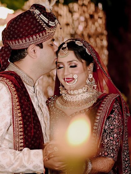 A tender moment between the bride and groom on their wedding day. The groom's gentle kiss on her forehead is a timeless expression of love and care.