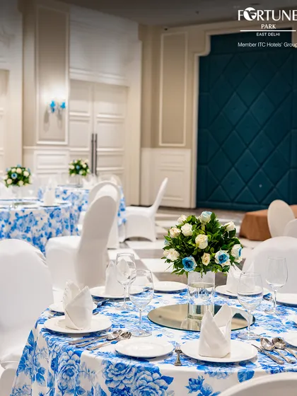 This detailed shot showcases the elegant table decor for a celebration. The combination of white and blue roses in the centerpiece perfectly complements the patterned tablecloths, adding a touch of refined beauty to the setting.