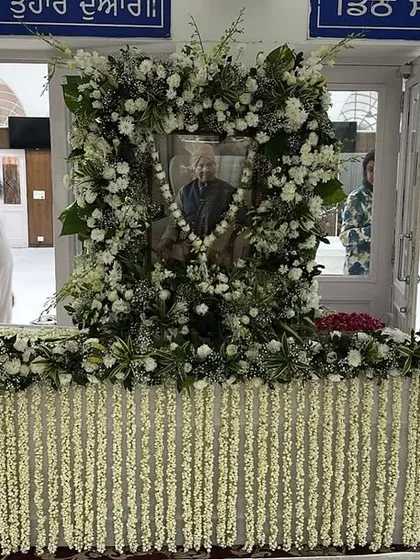 A respectful floral setup for a prayer meeting. The portrait is framed with fresh white flowers, and the table is adorned with jasmine strings, creating a peaceful ambiance for remembrance.