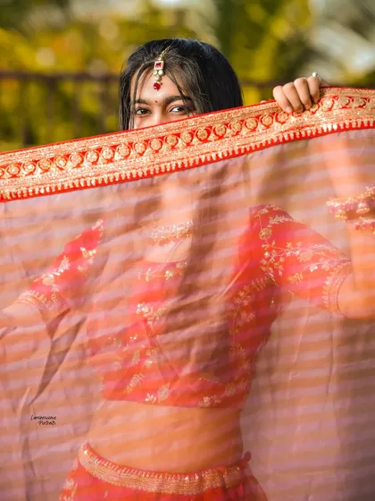 A peek-a-boo shot of the bride, her eyes playfully visible through her sheer red dupatta, adding a touch of mystery and fun.