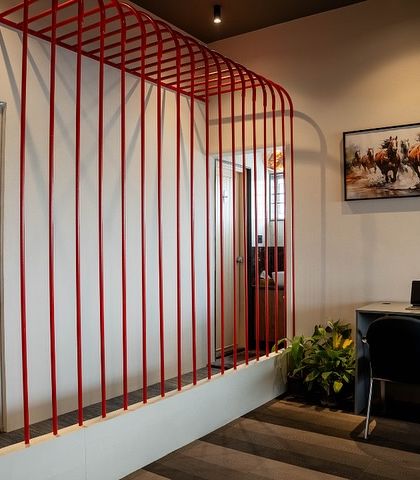 This open workstation is defined by a minimalist red metal frame, which acts as a light and airy space divider. It's a simple yet effective way to create zones in an open-plan office.