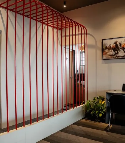 A simple yet effective workspace created using a red pipe-like partition. This minimalist approach defines a personal work area without closing it off, maintaining the open and collaborative feel of the office.