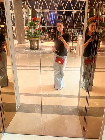 A mirror selfie capturing a simple yet chic outfit: a classic black t-shirt tucked into wide-leg jeans, accented with a small red crossbody bag for a pop of color. It's an easy, go-to look for any day.