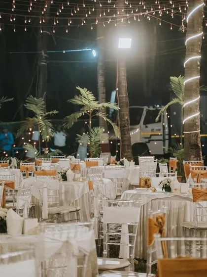 A clean and elegant white-themed reception seating arrangement. The simple color palette allows the warm glow of the string lights to create a romantic and inviting ambiance.