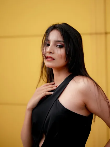 A striking portrait using a bold yellow wall as a backdrop. The simple background makes the model's expression and the clean lines of her black top the main focus of the image.