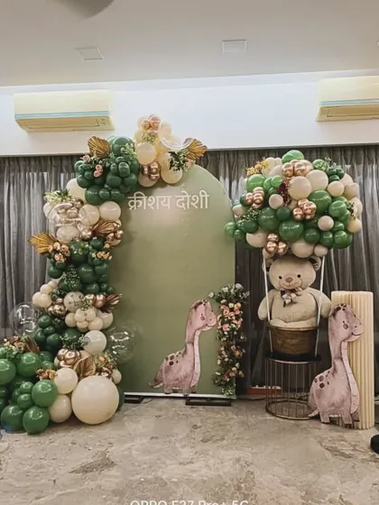 A cute dinosaur-themed decoration in sage green and beige. This setup includes dinosaur cutouts and a teddy bear in a hot air balloon basket, blending adventure with classic baby shower elements.