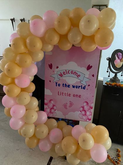A sweet 'Welcome to the world little one' sign on an easel, framed by a semi-arch of pastel pink and peach balloons for a baby's homecoming.