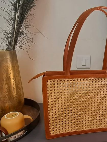 Our modern cane and vegan leather handbag, elegantly styled in a contemporary home setting. This structured bag combines traditional weaving with a sleek, professional design, making it a perfect accessory for the eco-conscious professional.