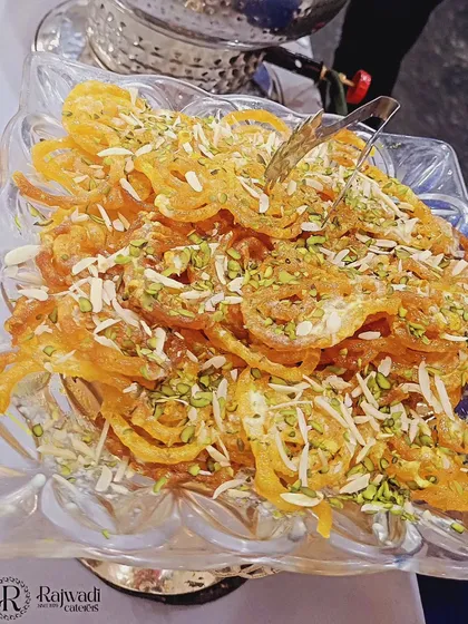 A close-up of fresh, crispy jalebis garnished with slivered almonds and pistachios. I ensure that even classic Indian sweets are presented beautifully, making them a highlight of the dessert counter.