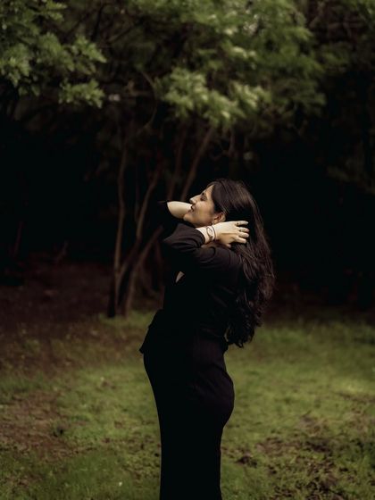 A dramatic and artistic solo portrait in the woods. The mom-to-be is in silhouette, looking up with her hands behind her head, creating a powerful and elegant shape.
