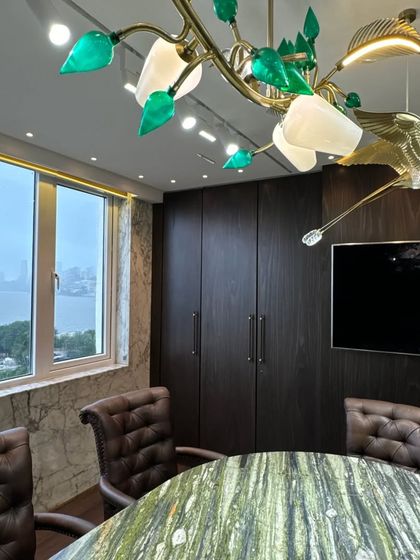The details make the design. This custom chandelier, featuring brass birds and green glass leaves, adds a touch of nature-inspired artistry to a corporate conference room, beautifully contrasting with the dark wood paneling.