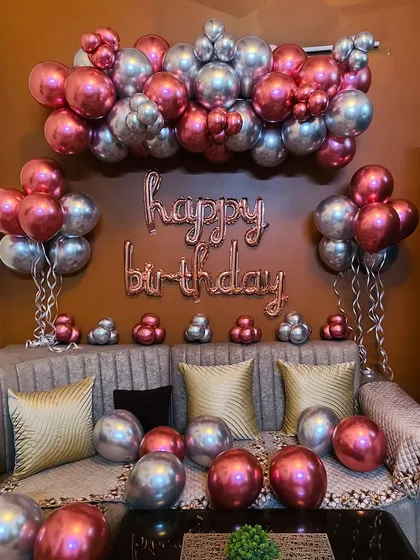 A simple yet chic living room decoration. This setup uses chrome balloons in rose gold and silver, arranged over a sofa with "happy birthday" foil letters.