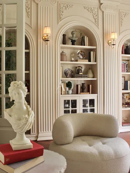 A detail shot of a classically Parisian reading nook. The fluted columns, arched bookshelf, and sculptural armchair create a corner that is both beautiful and functional.