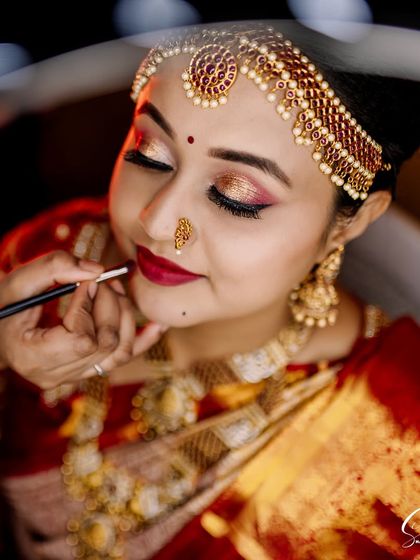 A behind the scenes moment, applying the final touches to the bride's lips. This look features dramatic eyes and a deep red lip, perfect for a traditional ceremony.