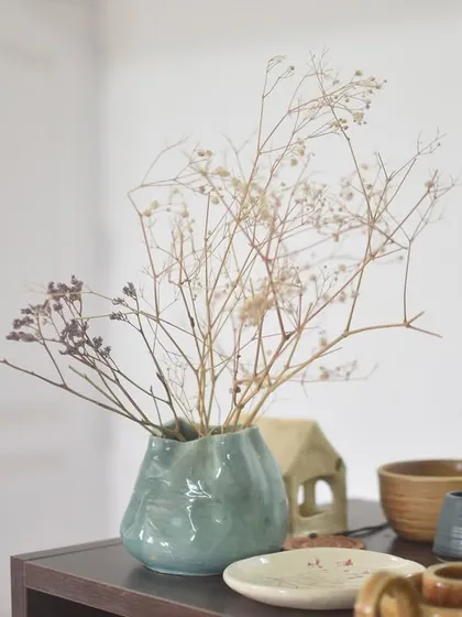 A finished, nature-inspired vase holding dried flowers, sitting beautifully on a shelf in my studio. This is the kind of simple elegance I love to create.