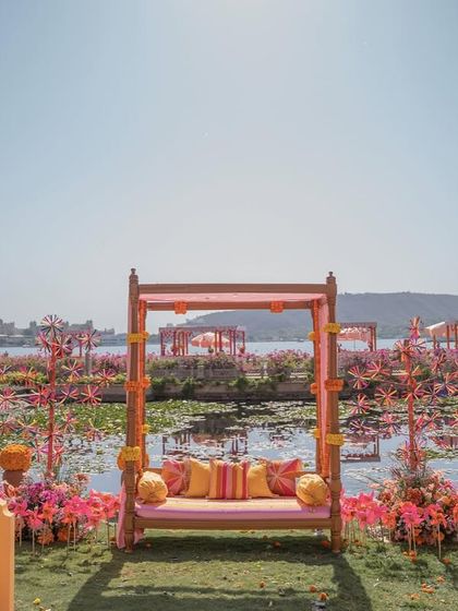 The main seating for the couple, a traditional swing or 'jhoola', set against the picturesque backdrop of Lake Pichola, surrounded by pinwheels and flowers.