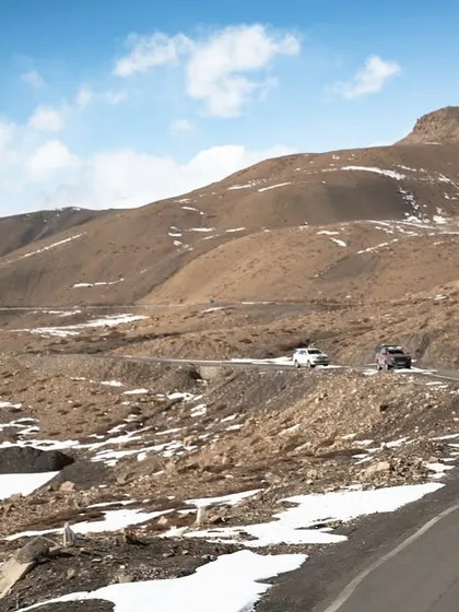 A convoy of 4x4s, led by a lime green Suzuki Jimny, snakes its way along a road carved into a barren mountainside. This photo is perfect for documenting group expeditions and off-road travel clubs.