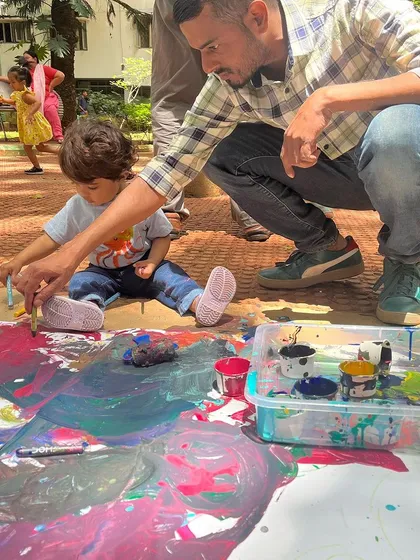 Art is a wonderful way for families to connect. In this moment from one of our parent-child workshops, a father and his toddler are creating a masterpiece together on a large canvas. We host sessions where you can bond with your child through shared creative exploration.