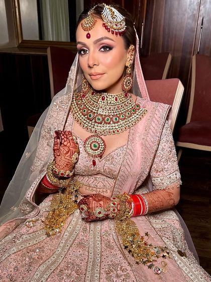 The bride holds her kaleeras, giving a closer look at her detailed henna and radiant makeup. The look is soft, romantic, and perfectly suited for her wedding day.