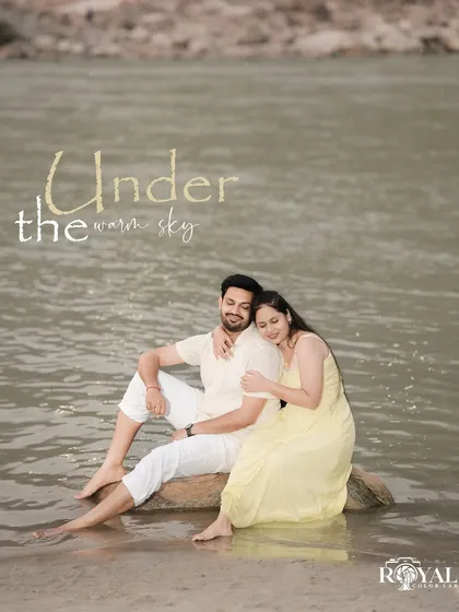 A serene portrait of a couple sitting on a rock by the river under a warm sky, capturing a peaceful moment.