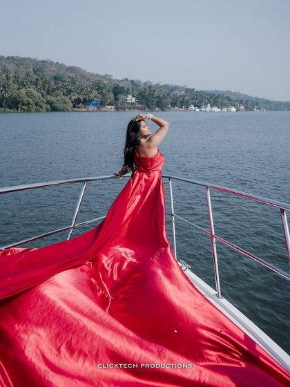 A striking pose by the bride-to-be on a yacht, her long red gown trailing behind her, capturing the essence of a glamorous destination photoshoot.