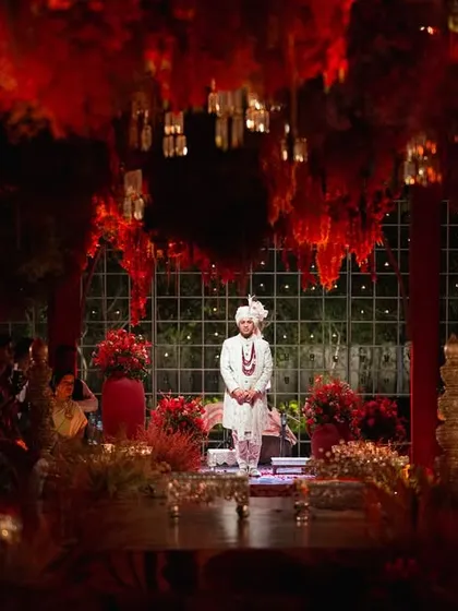 The groom waits at the magnificent red-themed mandap, a picture of anticipation and joy. The entire space was designed to build emotion, with layers of light and florals creating a world of romance for this unforgettable moment.