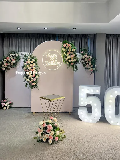 Elegance is key for milestone celebrations like a 50th birthday. This design uses beautiful artificial floral arrangements, a clean backdrop with a neon sign, and large marquee numbers for a timeless and sophisticated look.