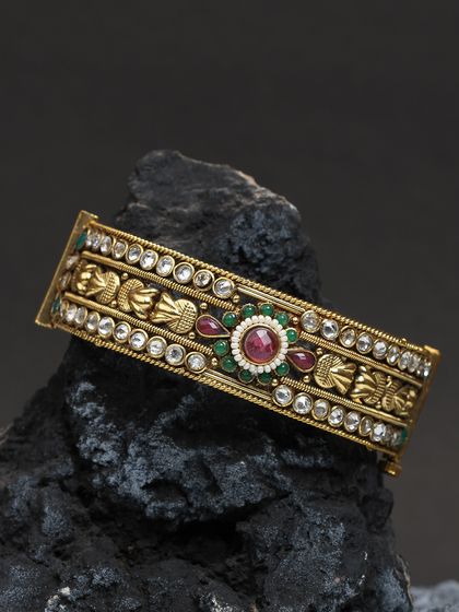 A traditional broad kada bangle with intricate carvings and kundan work.