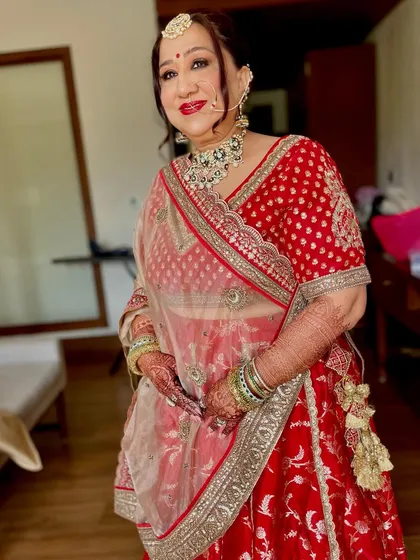 A traditional look for the mother of the bride in a classic red lehenga. The makeup is timeless, with a bright red lip and defined eyes, ensuring she looks regal and beautiful.