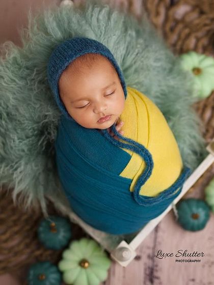 The same baby in a different setup, surrounded by decorative pumpkins that match the teal and yellow color scheme.